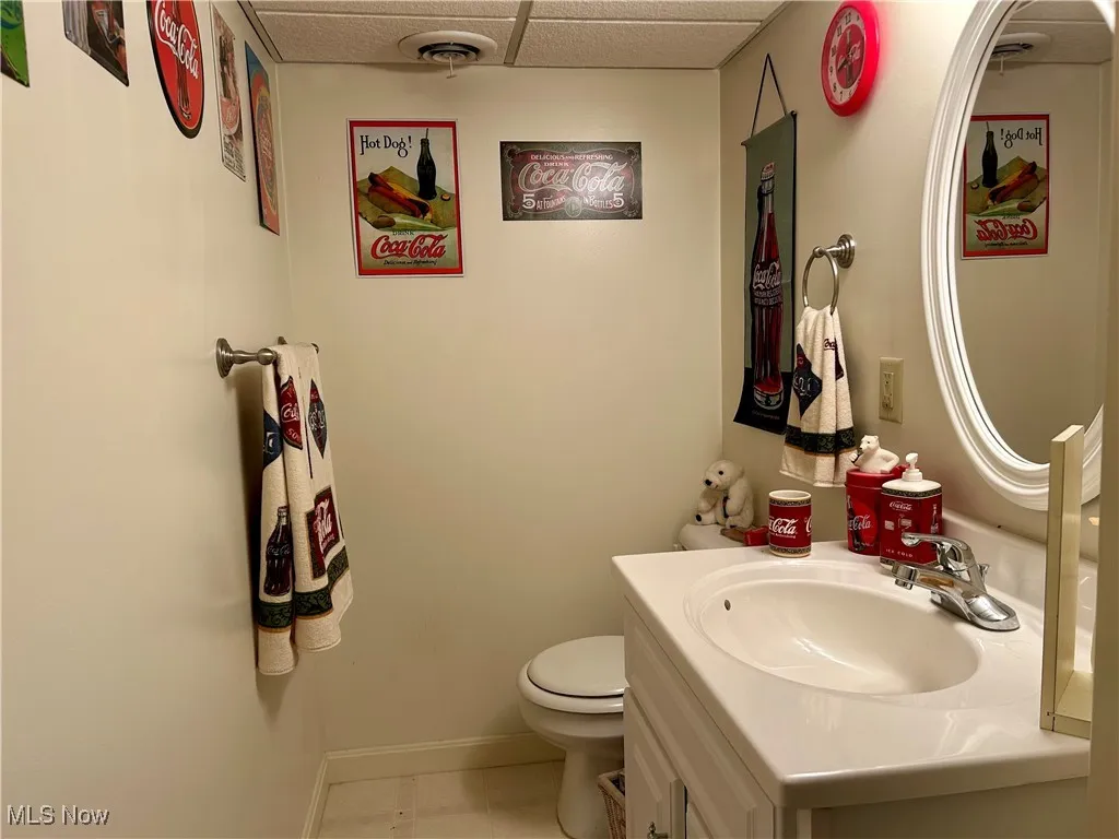 Half bath with vanity in the lower level, a drop ceiling, and light tile patterned floors