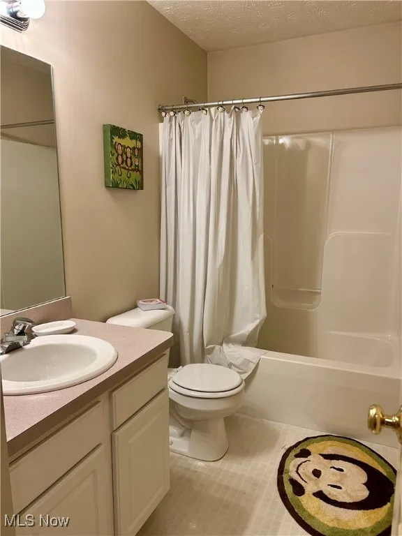Full bathroom with a textured ceiling, light tile patterned floors, vanity, and shower / tub combo