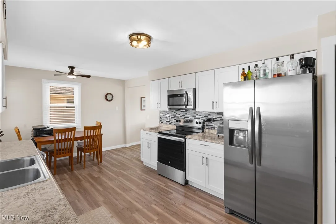 Kitchen with appliances with stainless steel finishes, tasteful backsplash, white cabinets, and light wood-style flooring