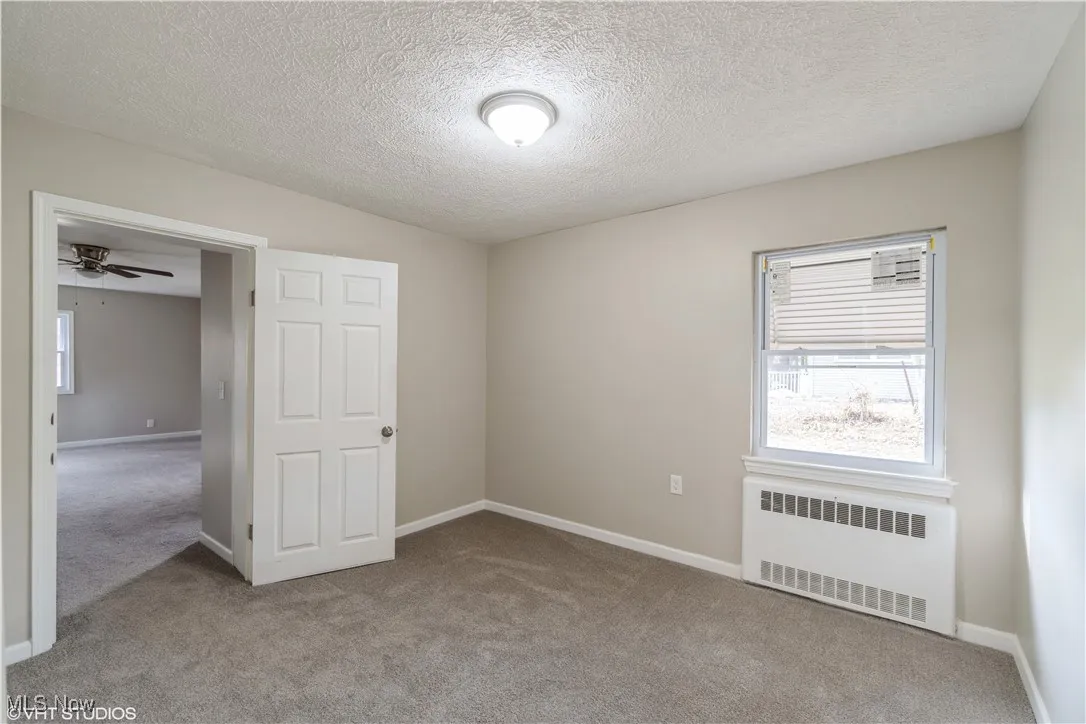 Unfurnished bedroom with radiator, carpet floors, and a textured ceiling