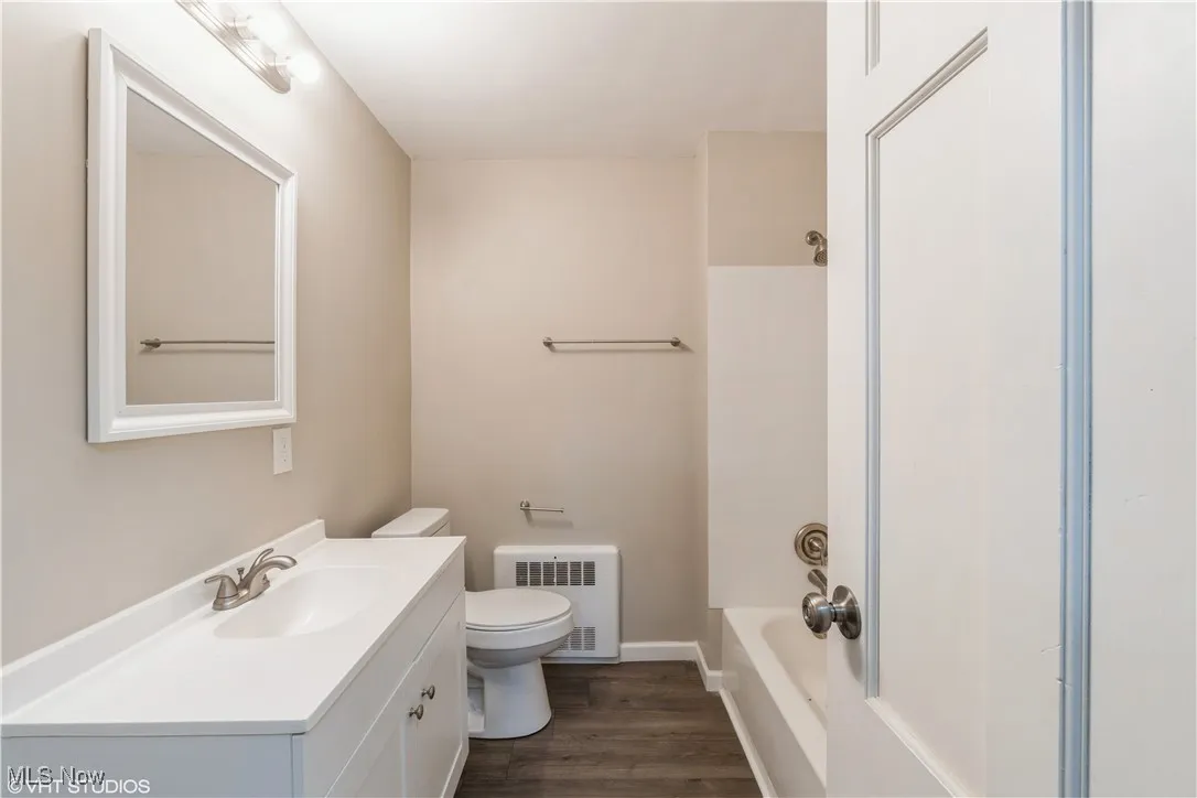 Full bathroom with dark wood-style floors, radiator heating unit, vanity, and tub / shower combination