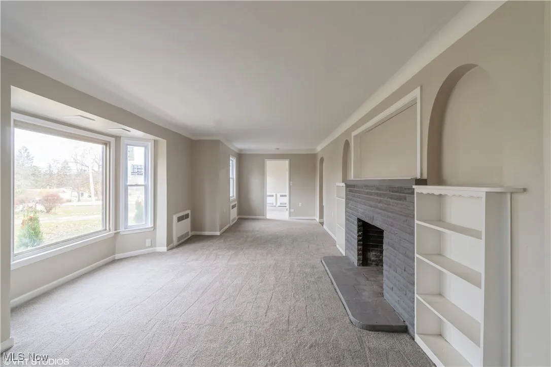 Unfurnished living room with a fireplace, carpet floors, and crown molding