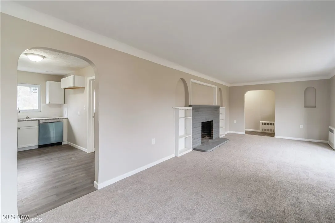 Unfurnished living room with arched walkways, a fireplace, and carpet floors