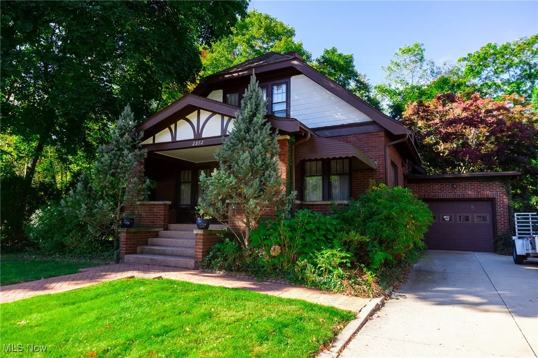 View of front facade featuring brick siding, a front yard, an attached garage, driveway, and covered porch