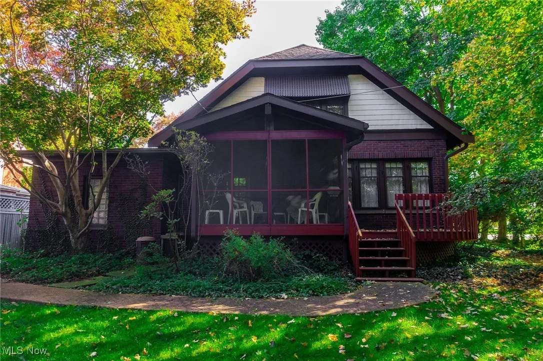 Rear view of property featuring a sunroom, brick siding, a deck, and stairs
