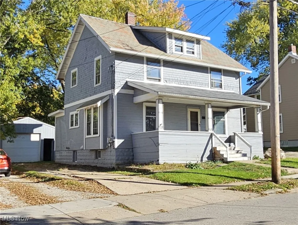 Traditional colonial style home with covered porch, a chimney, a detached garage, and driveway
