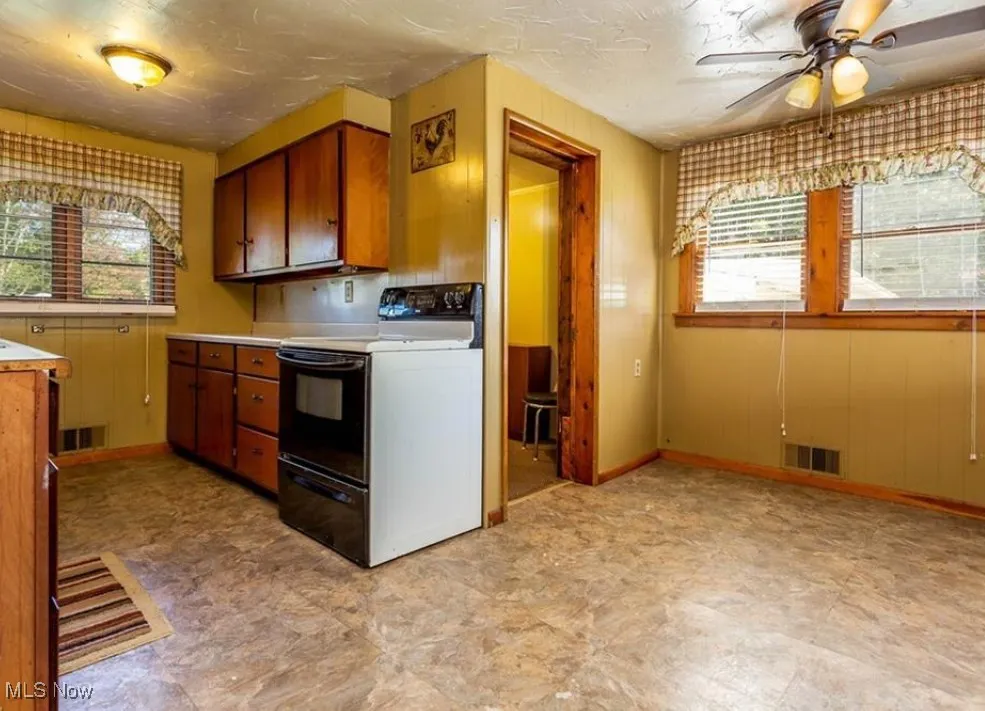 Kitchen featuring brown cabinets, range with electric stovetop, light countertops, healthy amount of natural light, and wooden walls