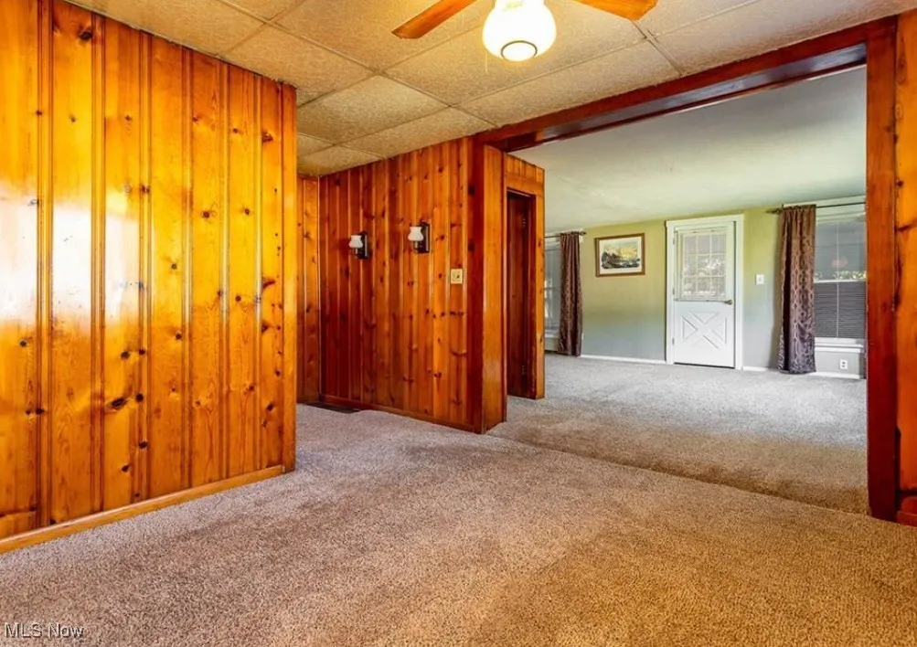 Spare room featuring carpet flooring, ceiling fan, wood walls, and a drop ceiling