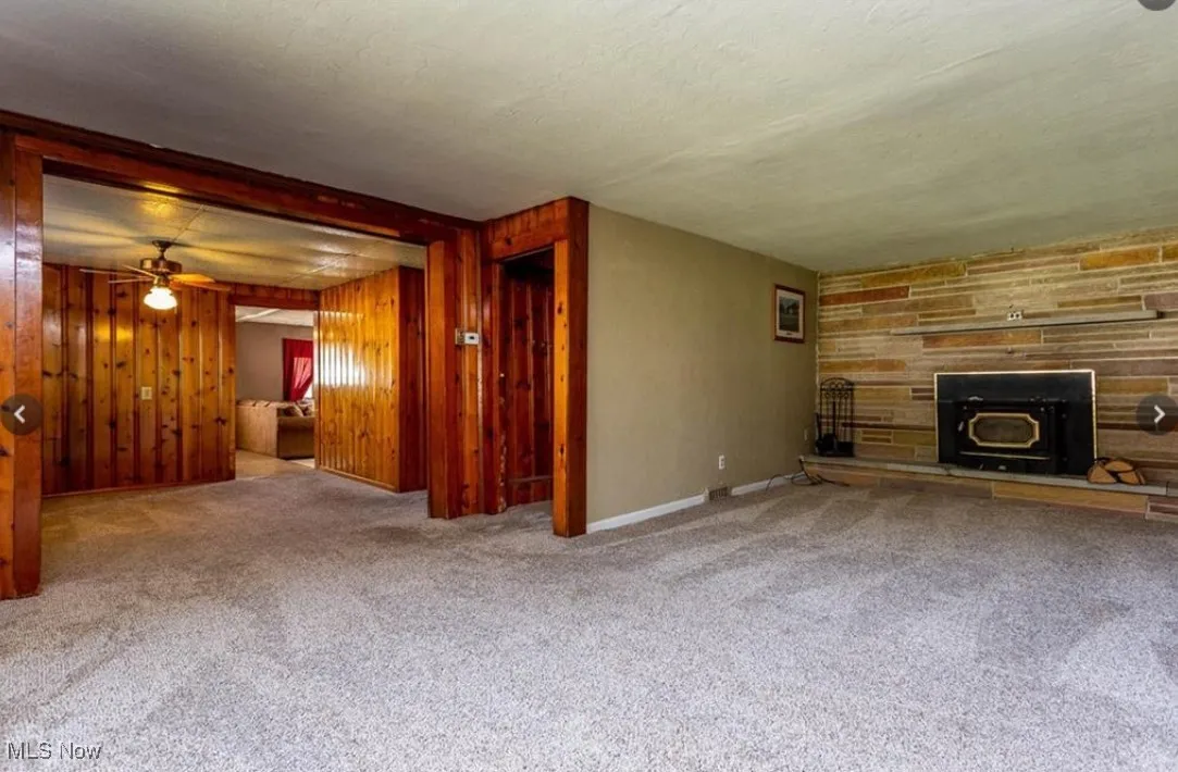 Unfurnished living room with carpet, a wood stove, wood walls, a ceiling fan, and a textured ceiling