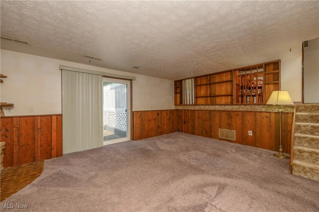 Unfurnished living room featuring wooden walls, a wainscoted wall, carpet, and a textured ceiling