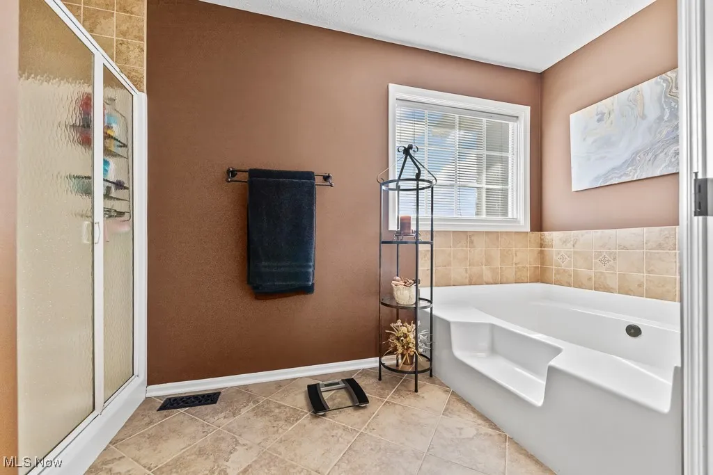 Bathroom featuring a stall shower, a garden tub, light tile patterned floors, and a textured ceiling