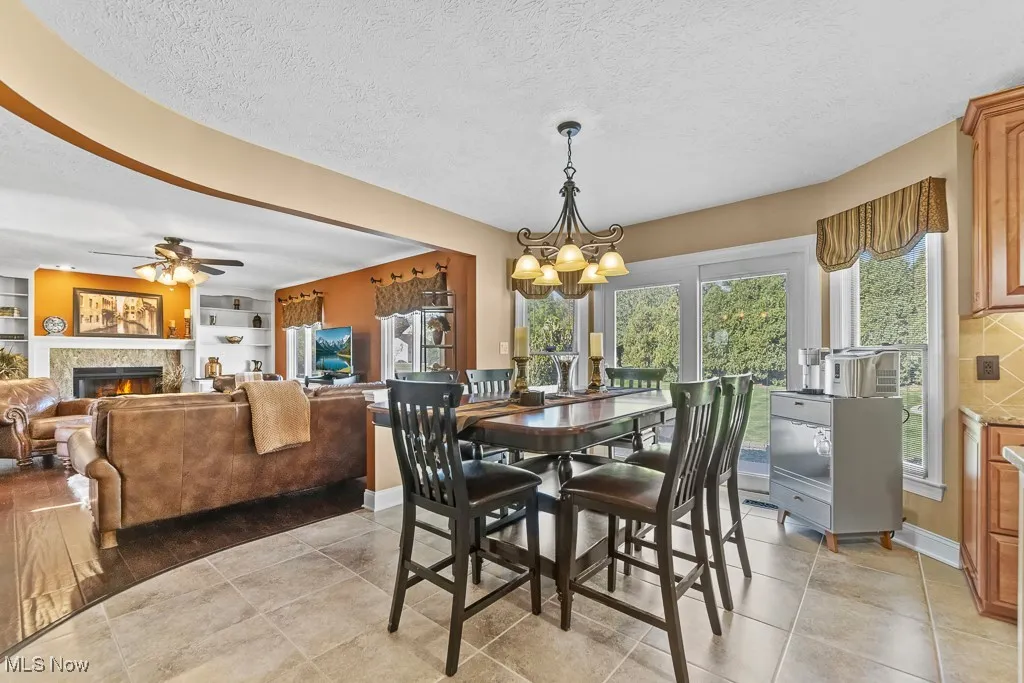 Dining space with a textured ceiling, a lit fireplace, built in features, a ceiling fan, and light tile patterned floors