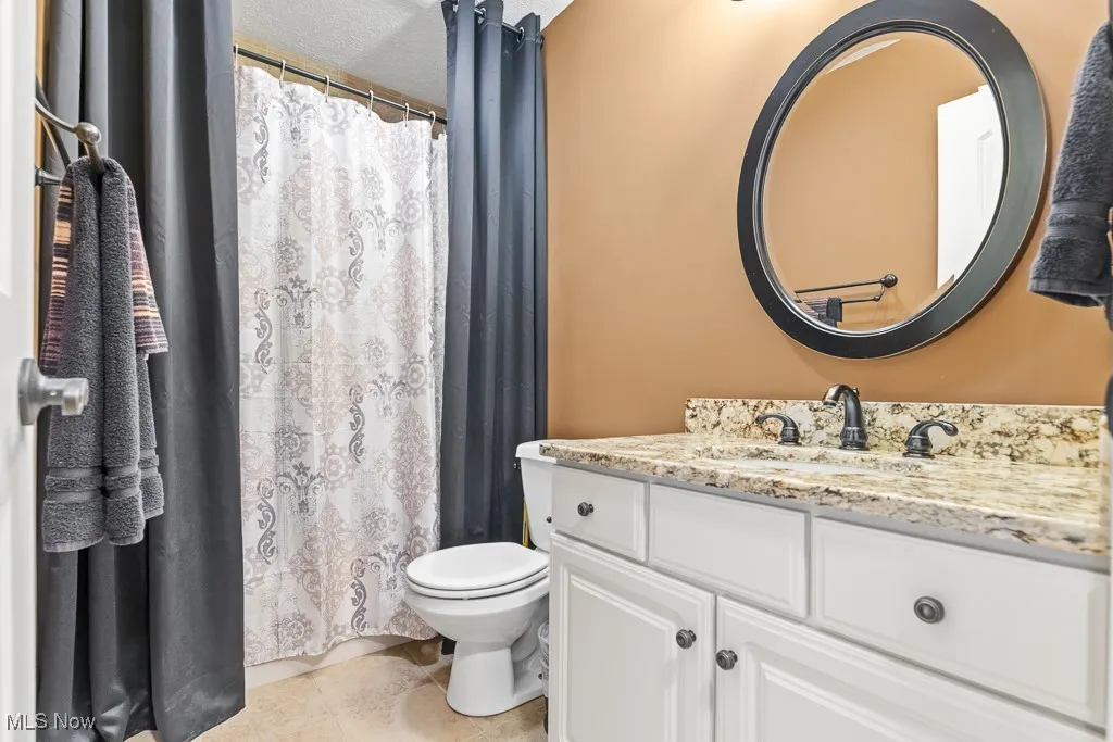 Bathroom with vanity, light tile patterned floors, a shower with curtain, and a textured ceiling