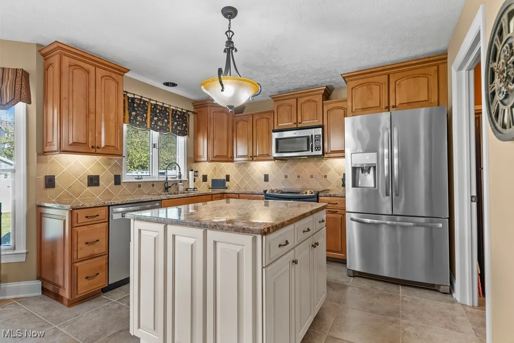 Kitchen with light stone counters, appliances with stainless steel finishes, pendant lighting, and brown cabinets