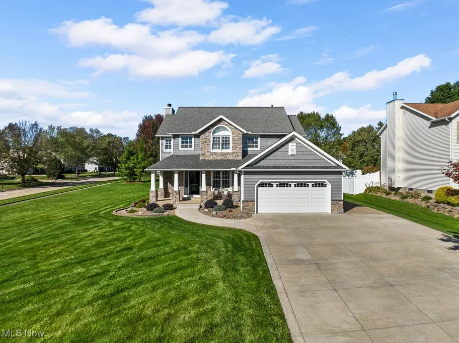 View of front of house featuring a porch, stone siding, driveway, a chimney, and an attached garage
