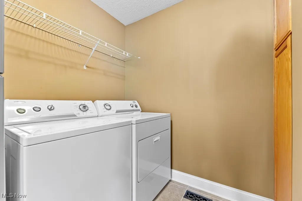 Laundry room featuring light tile patterned floors, washer and dryer, and a textured ceiling