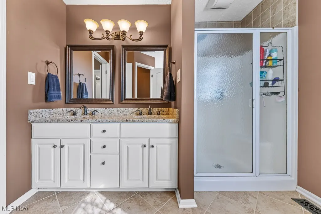 Bathroom with a shower stall, double vanity, light tile patterned floors, and a chandelier