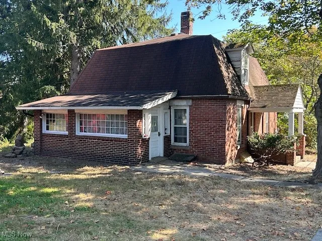 View of front of property featuring a chimney, brick siding, a gambrel roof, a shingled roof, and a front lawn