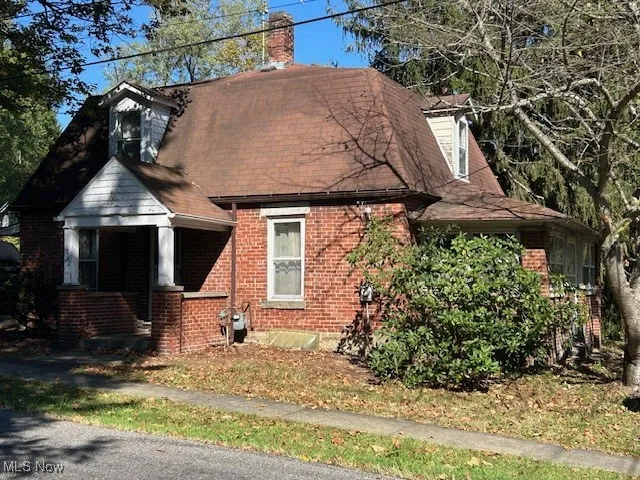 View of front of property with a chimney, brick siding, and a shingled roof