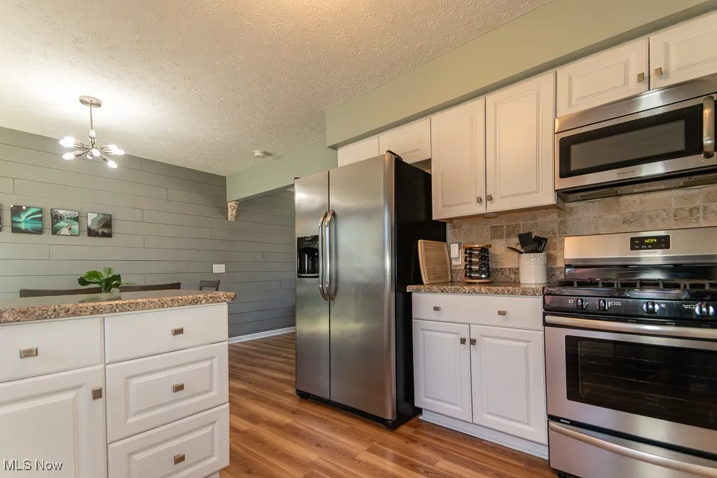 Kitchen with appliances with stainless steel finishes, white cabinets, light wood finished floors, light stone countertops, and a textured ceiling