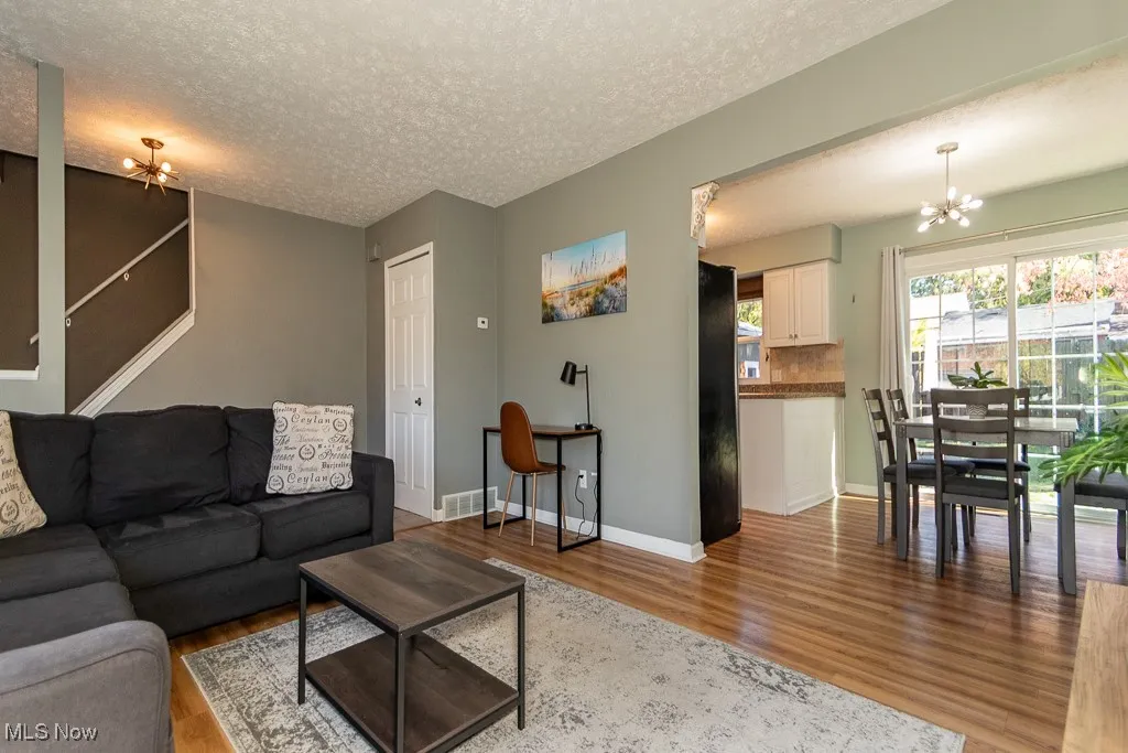 Living area featuring a chandelier, light wood-style floors, a textured ceiling, and stairs