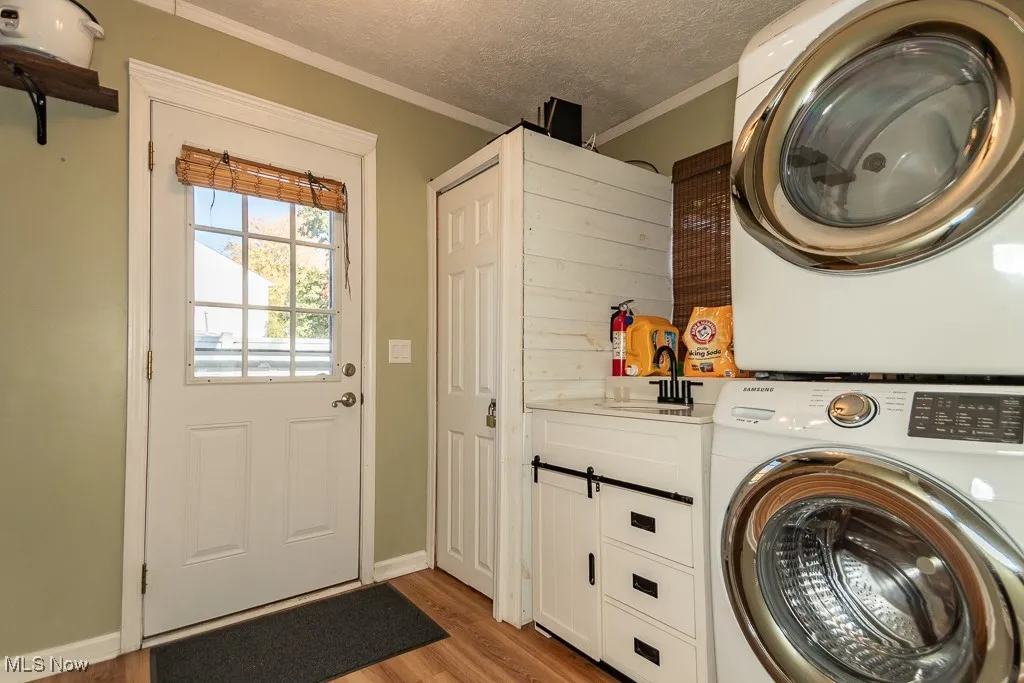 Washroom with a textured ceiling, ornamental molding, light wood-type flooring, estacked washer and dryer, and cabinet space