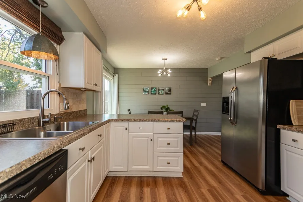Kitchen featuring decorative light fixtures, appliances with stainless steel finishes, a peninsula, dark wood-style floors, and white cabinetry