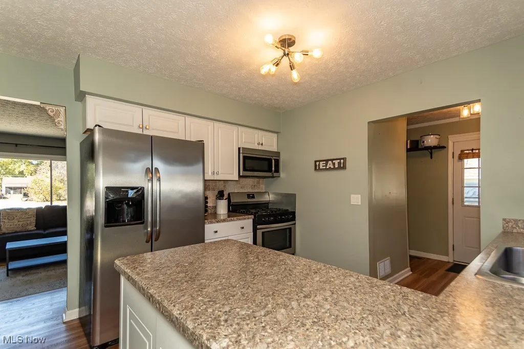 Kitchen with appliances with stainless steel finishes, white cabinets, dark wood finished floors, a textured ceiling, and light countertops