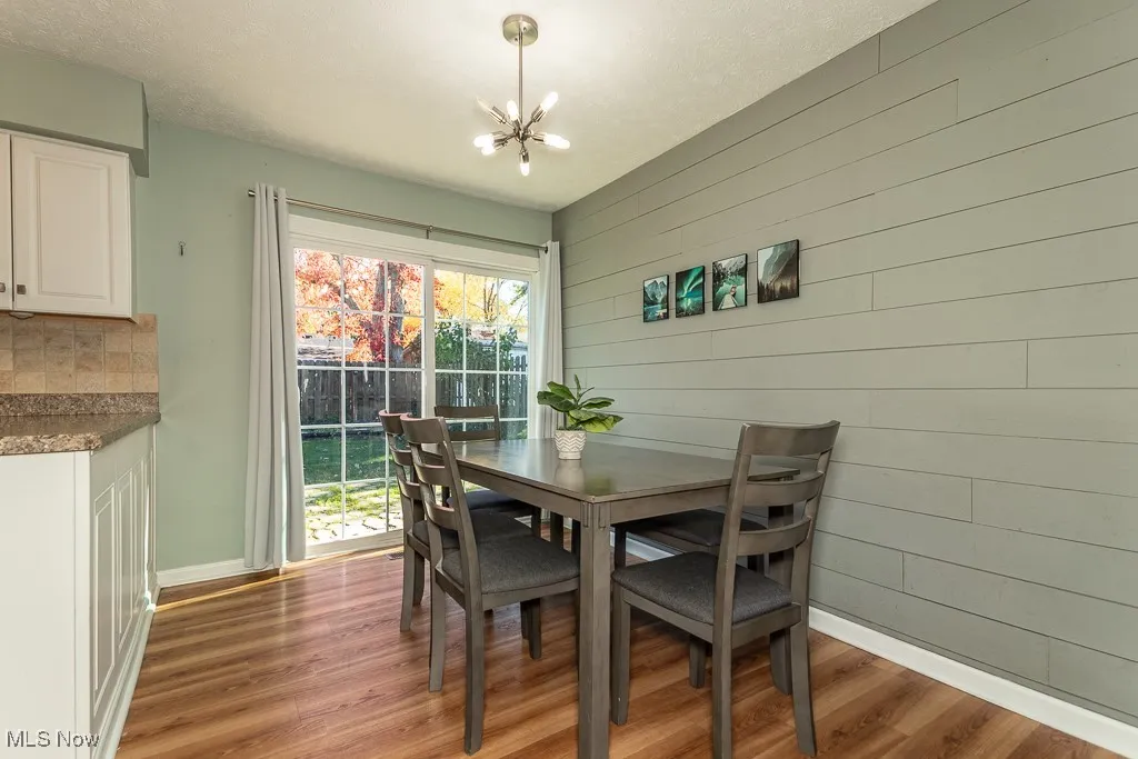 Dining space featuring light wood-style floors, a textured ceiling, a chandelier, and wood walls