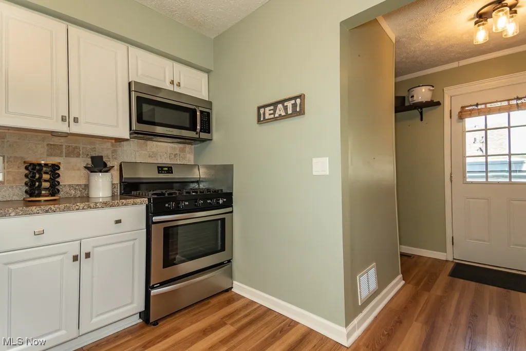 Kitchen with white cabinetry, appliances with stainless steel finishes, a textured ceiling, light wood-style flooring, and decorative backsplash