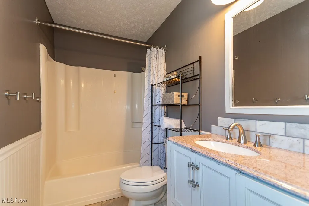 Bathroom with a textured ceiling, vanity, and shower / tub combo with curtain