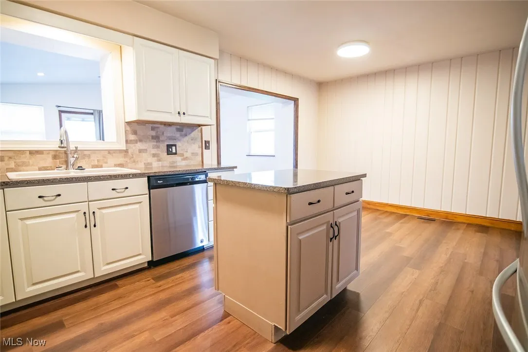 Kitchen featuring dark wood finished floors, dishwasher, backsplash, and a center island