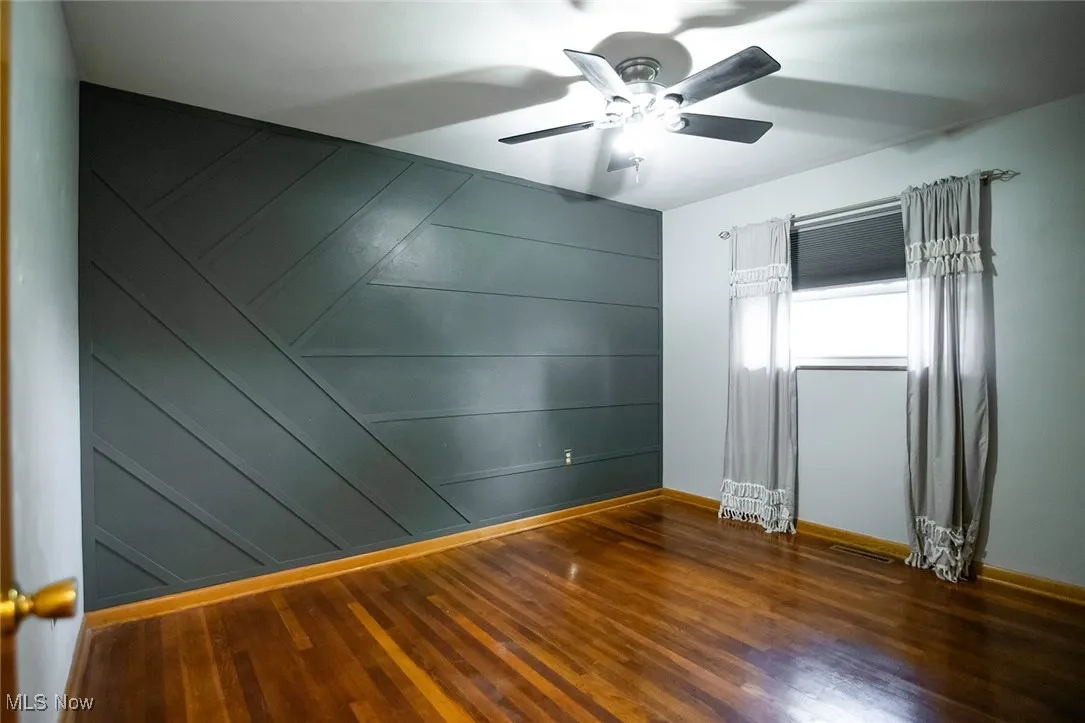 Spare room featuring wood finished floors, ceiling fan, and a decorative wall