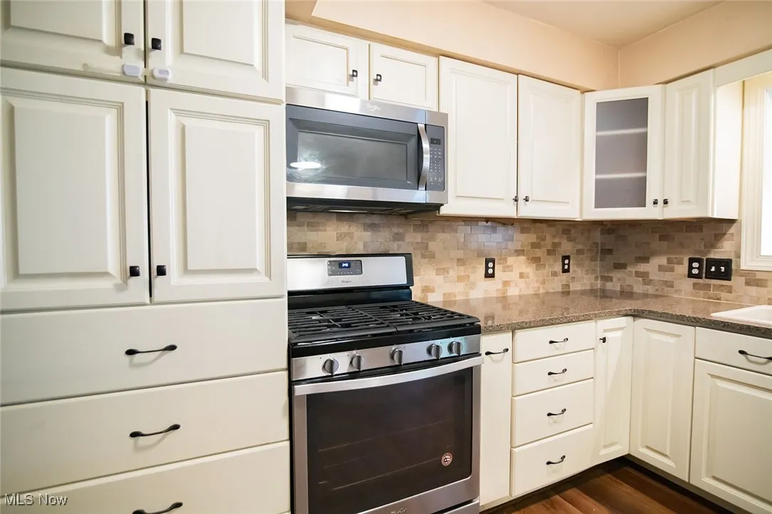 Kitchen with appliances with stainless steel finishes, tasteful backsplash, white cabinetry, and glass insert cabinets