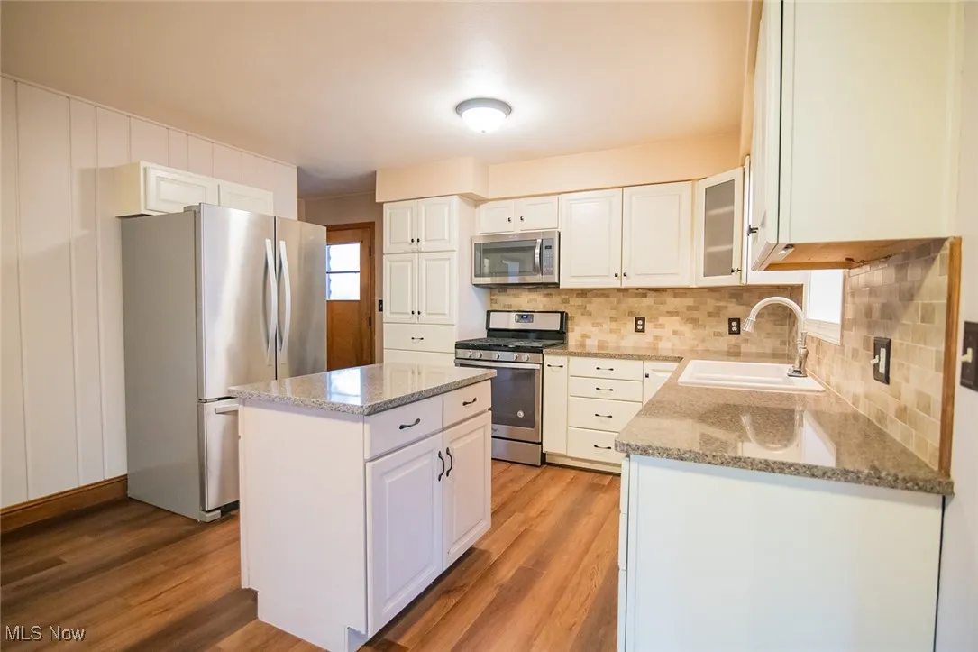 Kitchen featuring appliances with stainless steel finishes, white cabinetry, light stone counters, backsplash, and a center island
