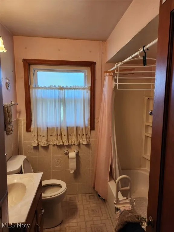 Full bathroom with vanity, shower / tub combo, tile walls, and light tile patterned flooring