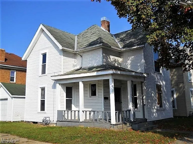 View of front of property featuring a porch, a chimney, and a garage