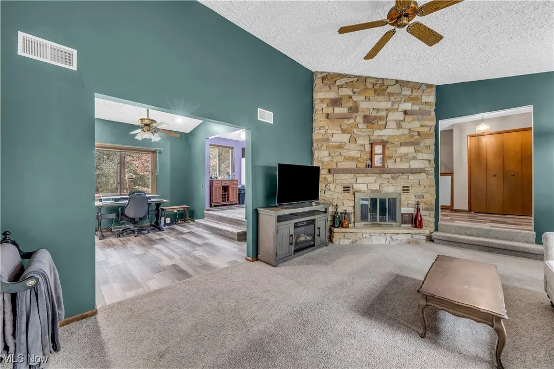 Living room featuring a ceiling fan, carpet flooring, a textured ceiling, a fireplace, and an office area