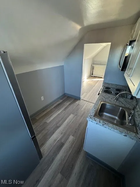 Kitchen featuring vaulted ceiling, dark wood-type flooring, radiator, white cabinets, and refrigerator