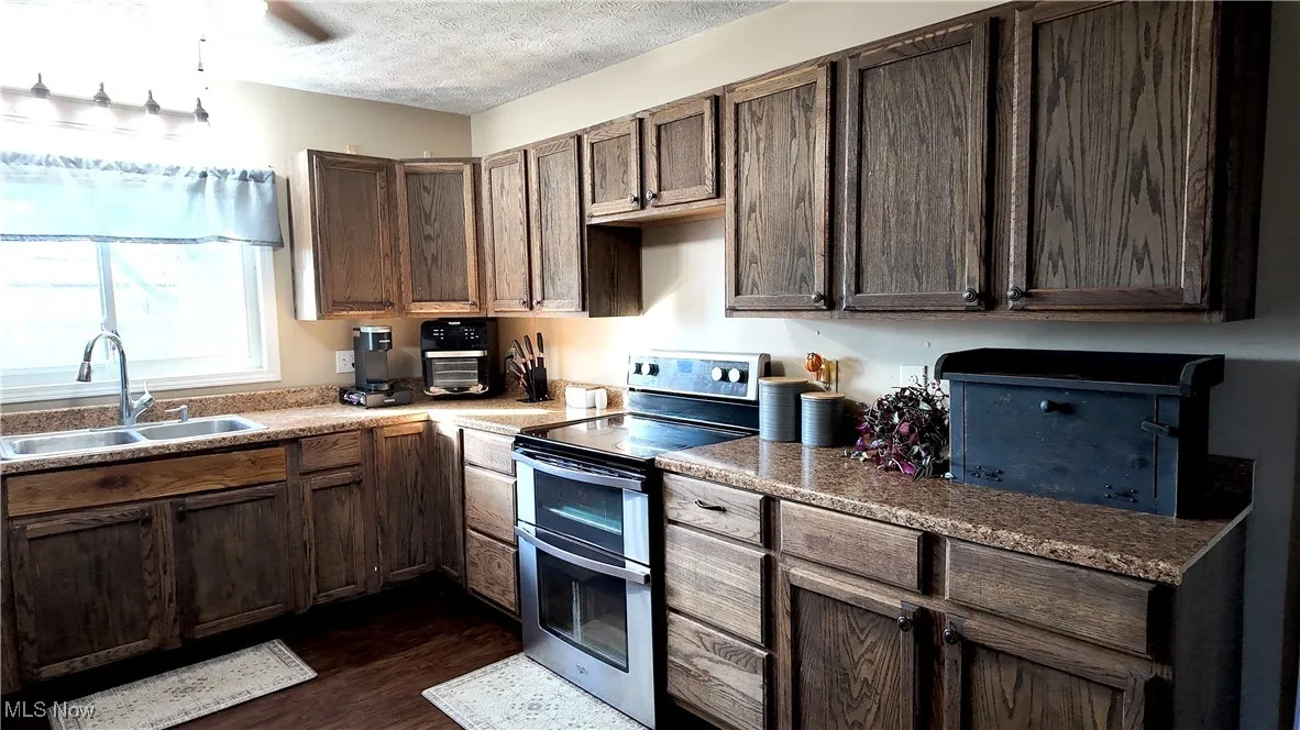 Kitchen featuring range with two ovens, a textured ceiling, dark wood-style flooring, dark brown cabinetry, and light countertops