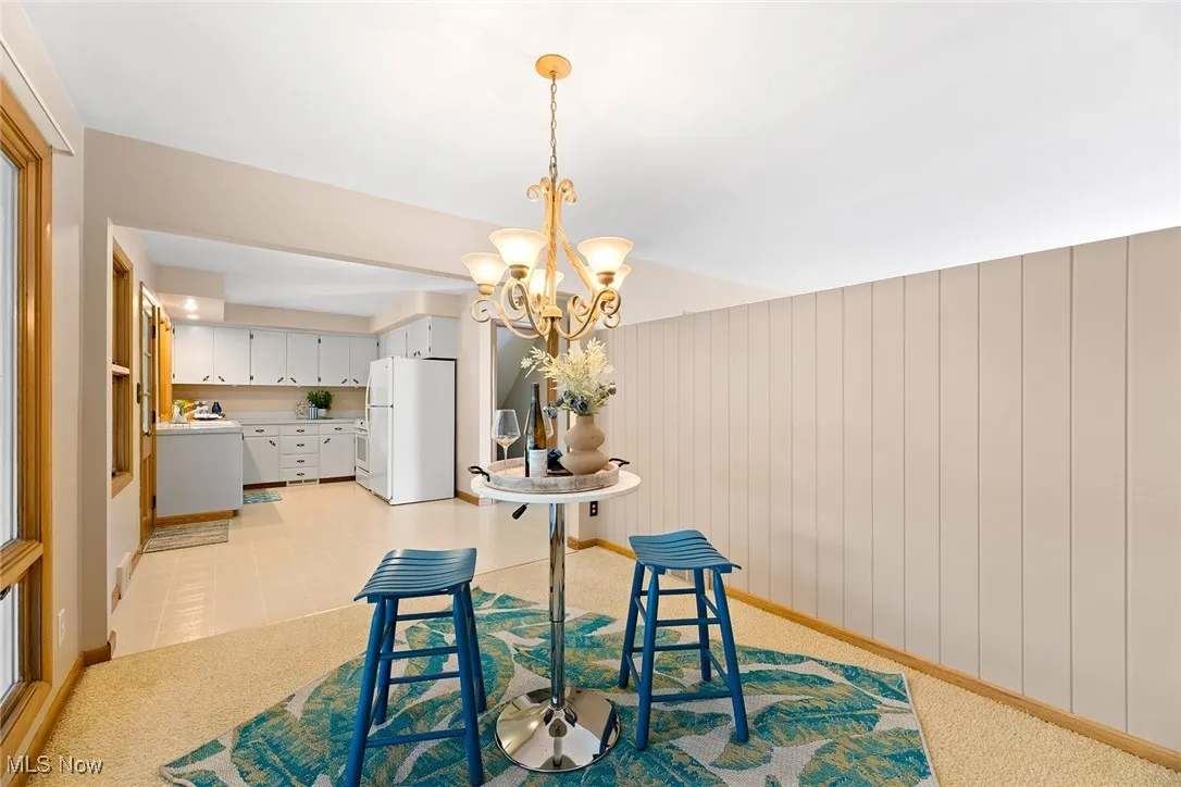 Dining area featuring a chandelier, wooden walls, light carpet, and light tile patterned floors