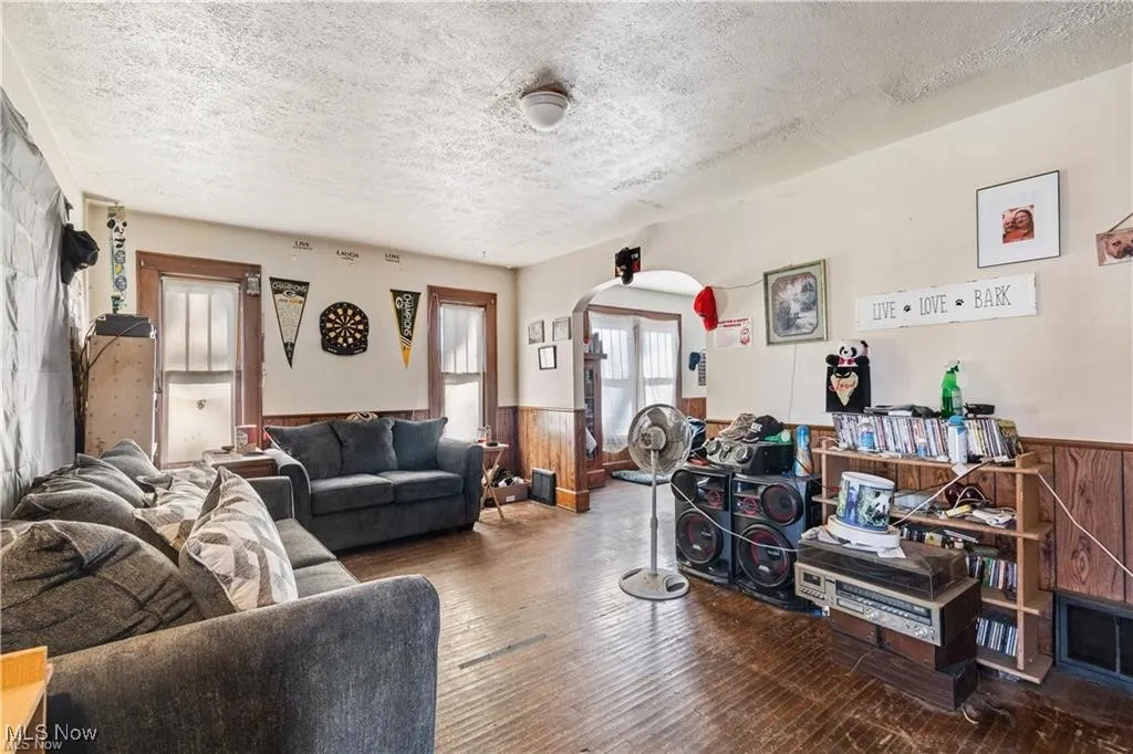 Living room featuring arched walkways, wood walls, hardwood / wood-style flooring, a textured ceiling, and wainscoting