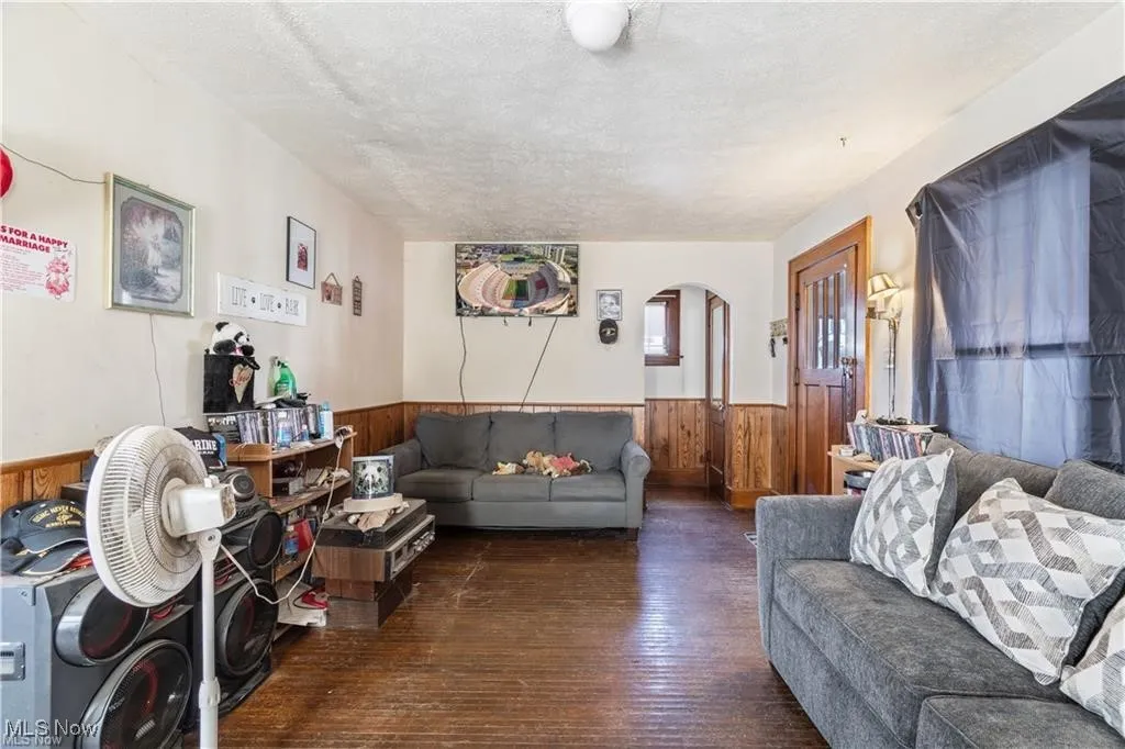 Living room featuring a textured ceiling, hardwood / wood-style floors, arched walkways, a wainscoted wall, and wooden walls