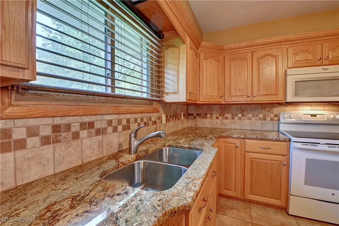 Kitchen featuring white appliances, backsplash, light stone counters, and light tile patterned floors