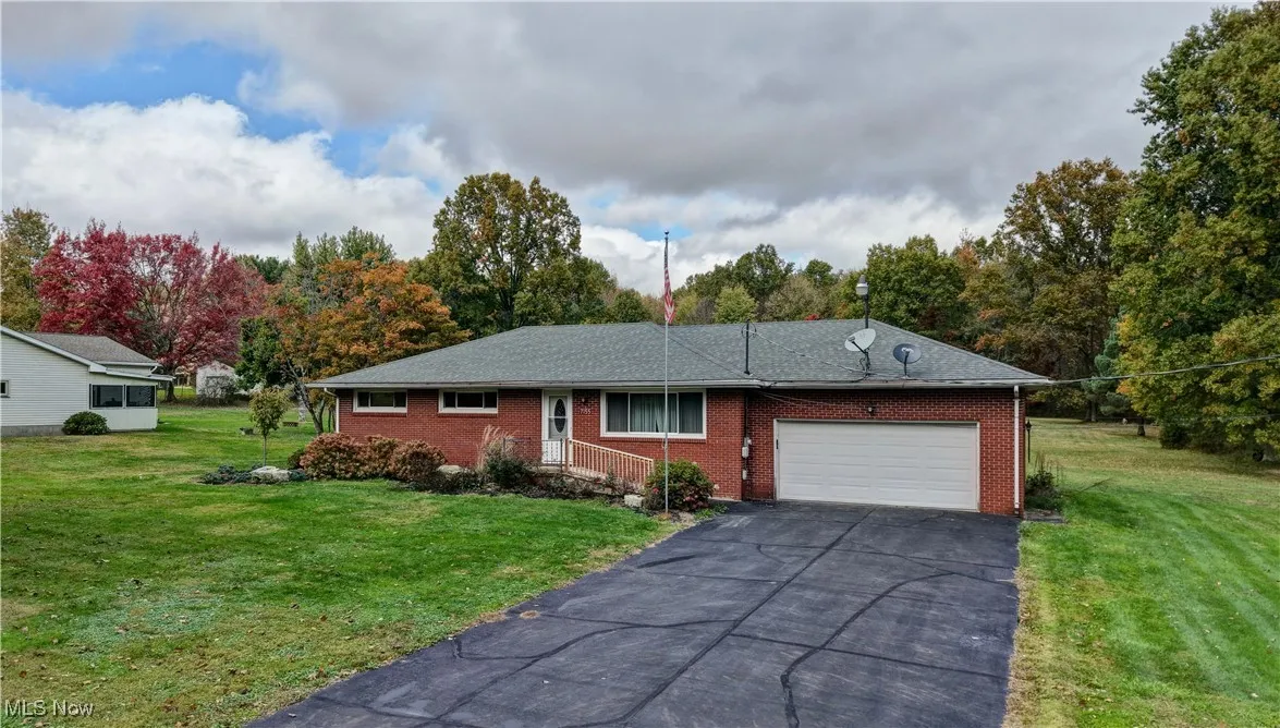 Single story home featuring a front lawn, a garage, brick siding, driveway, and view of wooded area