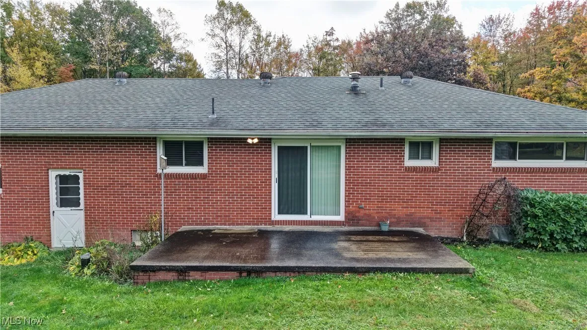 Rear view of house with a lawn, brick siding, and roof with shingles