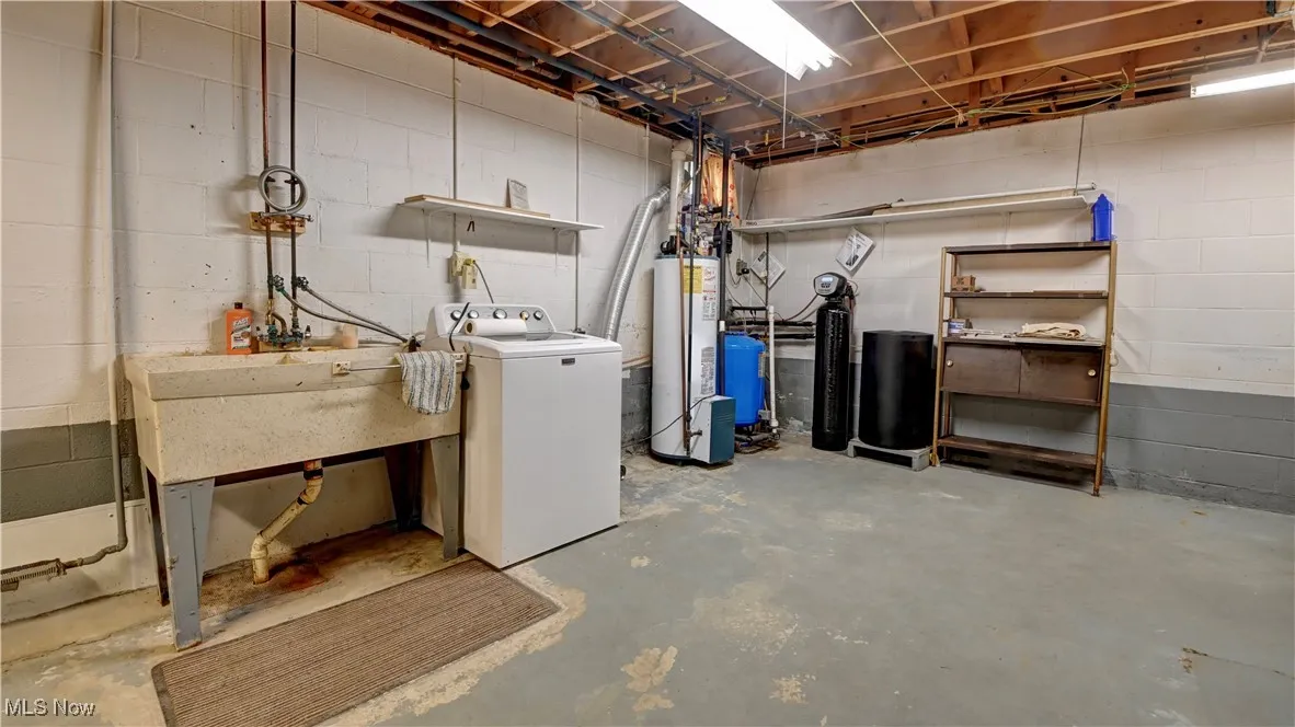 Unfinished basement with washer / clothes dryer, a water softener system, water heater, and a water pressure tank