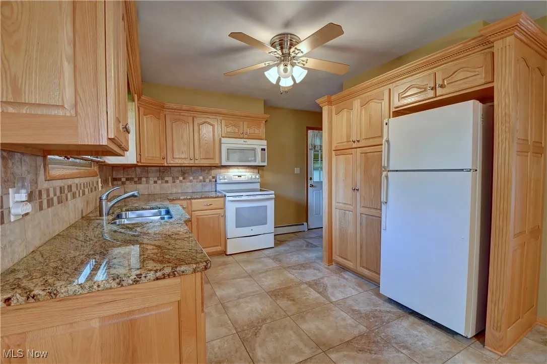 Kitchen featuring light brown cabinetry, white appliances, backsplash, light stone countertops, and ceiling fan