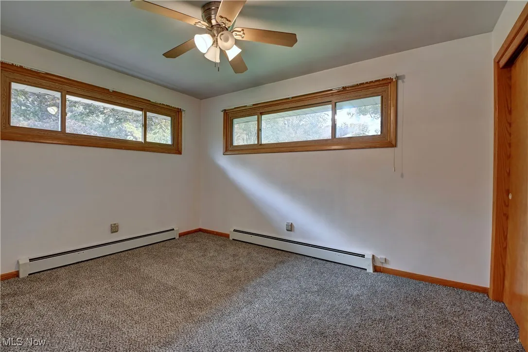 Empty room with baseboard heating, plenty of natural light, and carpet flooring