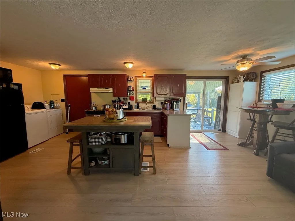 Kitchen featuring a textured ceiling, freestanding refrigerator, a peninsula, light wood-type flooring, and washing machine and clothes dryer